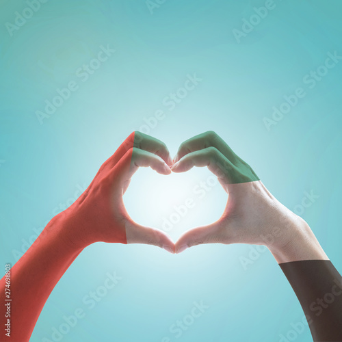 UAE, United Arab Emirate national flag pattern on people's hands in heart shape on blue mint sky background