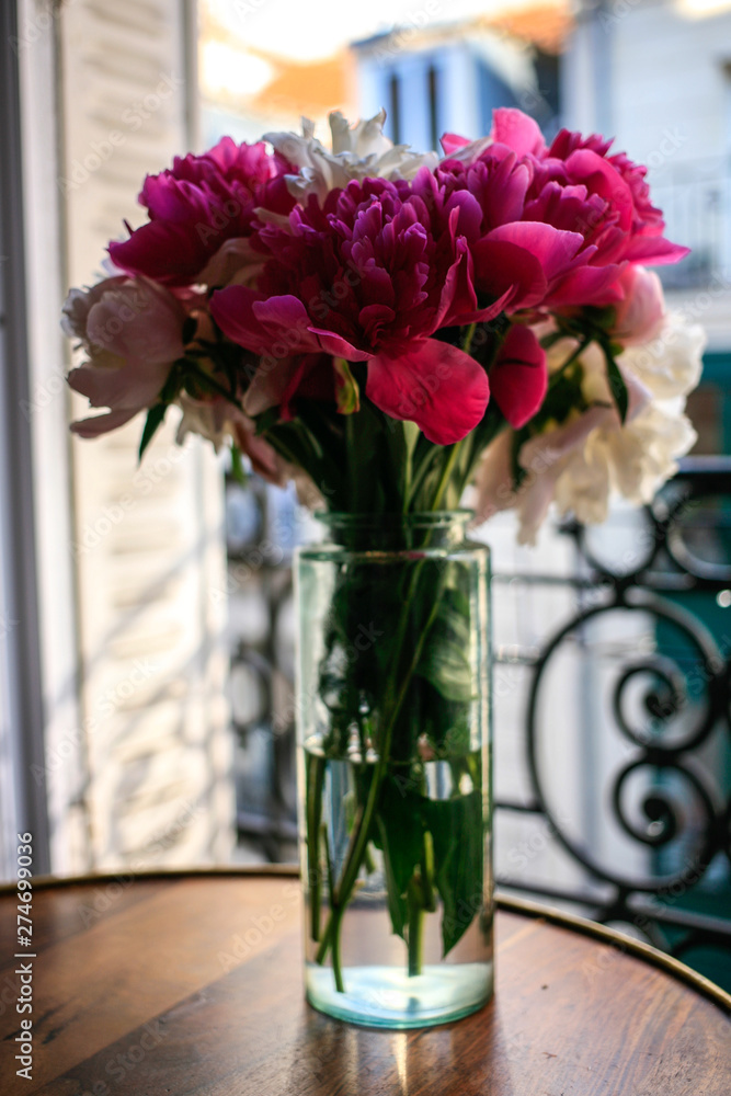 Gorgeous white and pink pions in a glass vase in sunset light in front of the open Parisian window Gorgeous white and pink pions in a glass vase in sunset light in front of the open Parisian window