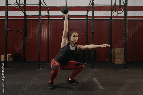 Crossfit woman doing overhead dumbbell squats at the gym.