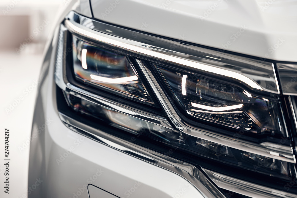 Close-up headlights of a modern white color car. Detail on the front light of a car. Modern and expensive car concept. The car is in the showroom