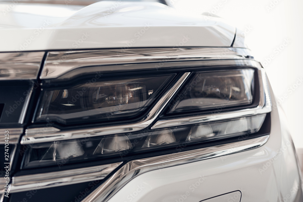 Close-up headlights of a modern white color car. Detail on the front light of a car. Modern and expensive car concept. The car is in the showroom