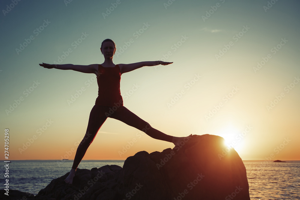 Yoga woman performs morning exercises on the seaside in the dawn.