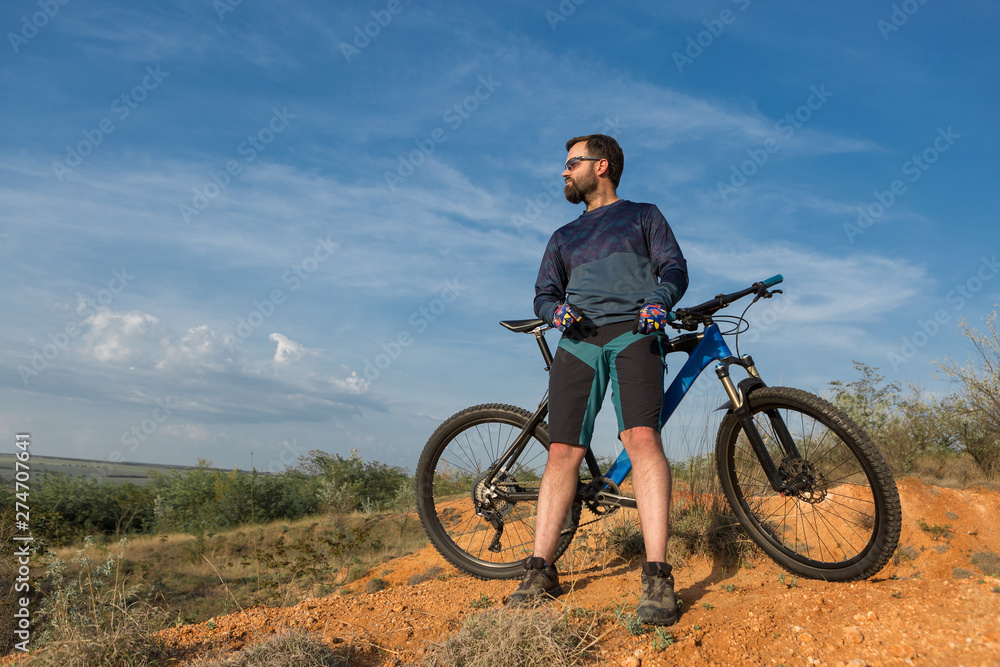 Cyclist in shorts and jersey on a modern carbon hardtail bike with an air suspension fork rides off-road on the orange-red hills at sunset evening in summer	