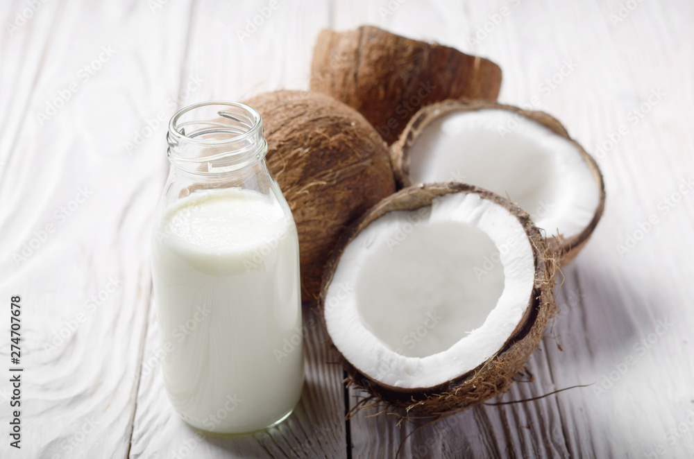 Milk or yogurt in glass bottle on white wooden table with coconut aside Milk or yogurt in glass bottle on white wooden table with coconut aside