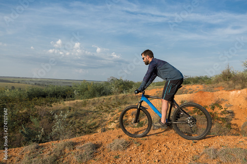 Cyclist in shorts and jersey on a modern carbon hardtail bike with an air suspension fork rides off-road on the orange-red hills at sunset evening in summer 