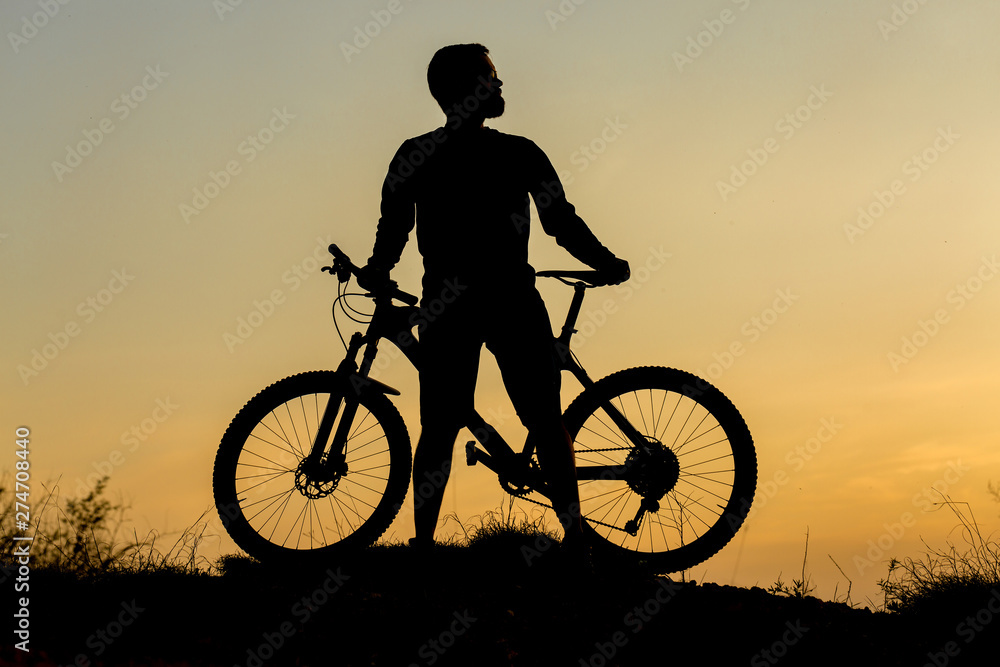 Obraz premium Cyclist in shorts and jersey on a modern carbon hardtail bike with an air suspension fork rides off-road on the orange-red hills at sunset evening in summer 