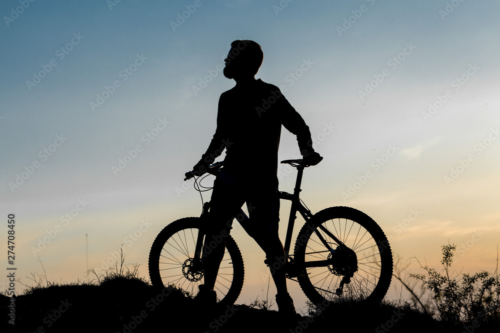 Cyclist in shorts and jersey on a modern carbon hardtail bike with an air suspension fork rides off-road on the orange-red hills at sunset evening in summer Cyclist in shorts and jersey on a modern carbon hardtail bike with an air suspension fork rides off-road on the orange-red hills at sunset evening in summer