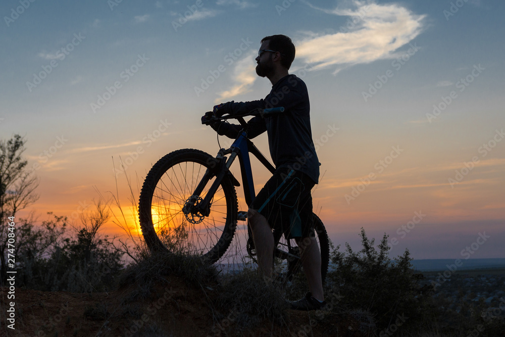 Obraz premium Cyclist in shorts and jersey on a modern carbon hardtail bike with an air suspension fork rides off-road on the orange-red hills at sunset evening in summer 
