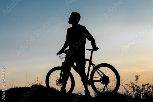 Cyclist in shorts and jersey on a modern carbon hardtail bike with an air suspension fork rides off-road on the orange-red hills at sunset evening in summer 