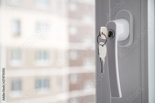 Handle with lock and key on the PVC window. Apartment house on the background. Closeup, selective focus photo