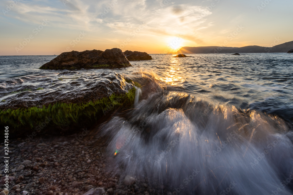 Obraz premium waves hits rocks during sunset. image contain soft focus and blue due to slow shutter