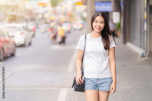 Portrait of Happy Asian young adult woman wearing white casual, short blue jeans smiling with teeth and walking on city street at sunset time. Bangkok Thailand. © visitr