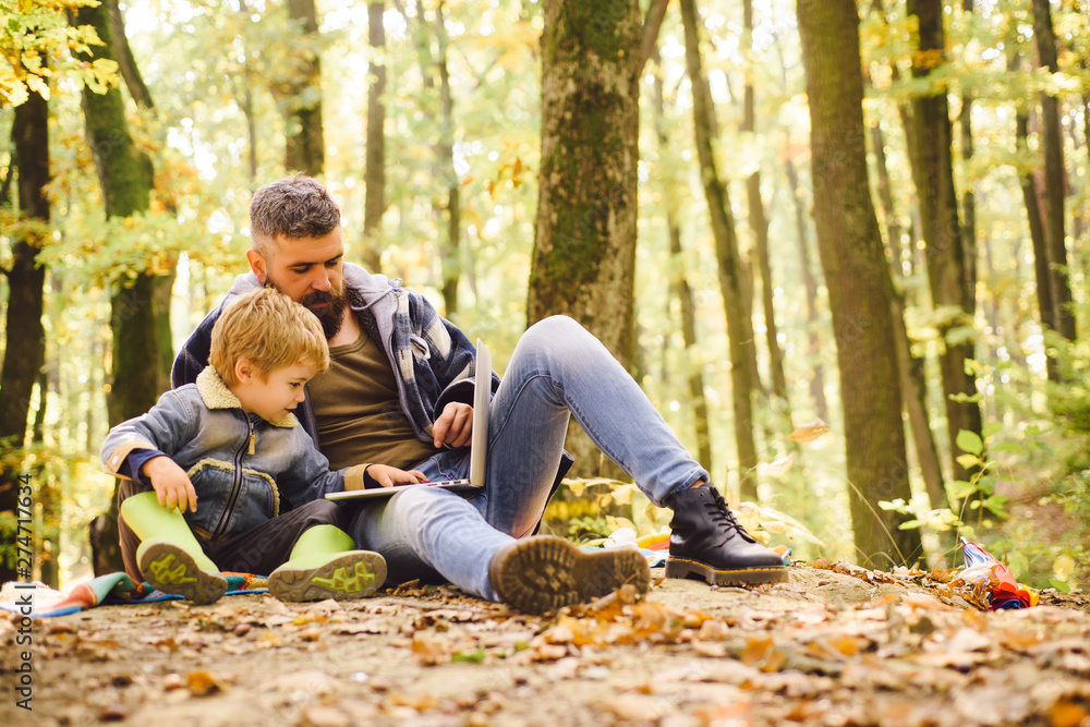 Fototapeta premium Modern family. Ecology lesson. Forest school and ecology education. Man bearded father and son with laptop in forest. Ecology upbringing. Father teaches son use modern technology. United with nature
