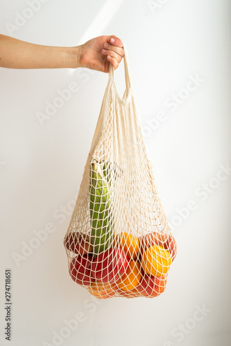 Female hand holding cotton string bag with fresh fruits and vegetables