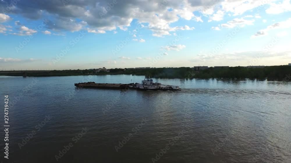 Aerial drone follow stacking shot of an empty garbage barge sailing across a river canal towards a bridge Aerial drone follow stacking shot of an empty garbage barge sailing across a river canal towards a bridge