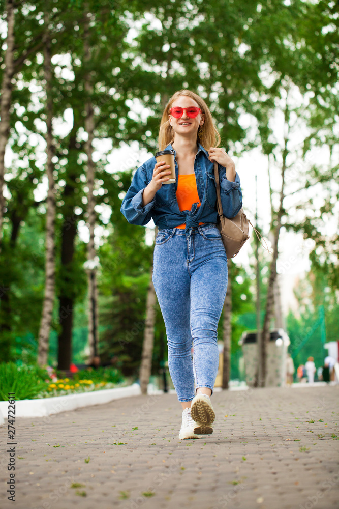 Fototapeta premium Young Blonde Girl in blue jeans walking in summer park