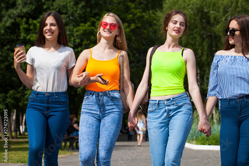 Four happy schoolgirls walking in summer park