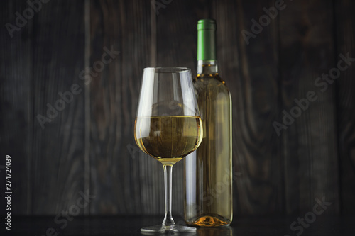 Transparent bottle of white dry wine on the table. White wine glass on a wooden background.