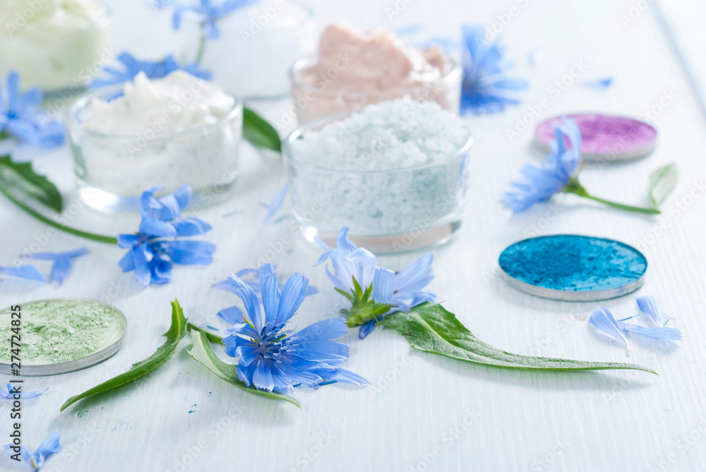 moisturizers, bath salts and powder compacts with blue chicory flowers on white wood table moisturizers, bath salts and powder compacts with blue chicory flowers on white wood table
