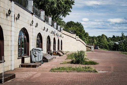 The pavement is red-brown in color  on the left is a one-story building with windows in the form of an arch  and trees and a cloudy sky are visible ahead.