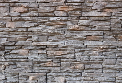 Dark gray and brown exterior wall cladding made of irregular natural stones. Stone paneling, background and texture.