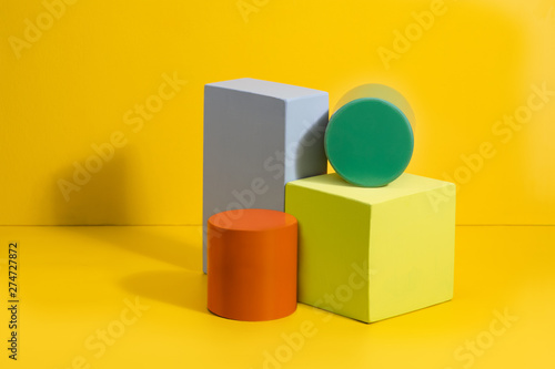 Geometric shapes in different colors on yellow background. Three-dimensional solid figures on colored paper.