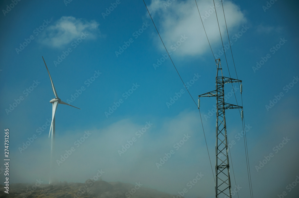 Wind turbines on hill with mist next to electric tower Wind turbines on hill with mist next to electric tower