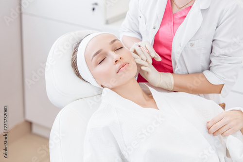 Close-up master cosmetologist makes injection of hiluronic acid in the face of a beautiful young woman. The concept of modern anti-aging procedures in the beauty salon