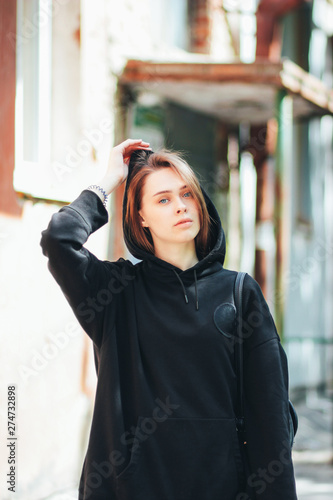 Candid portrait of young beautiful long hair girl fashion model hipster in black hoody on city street