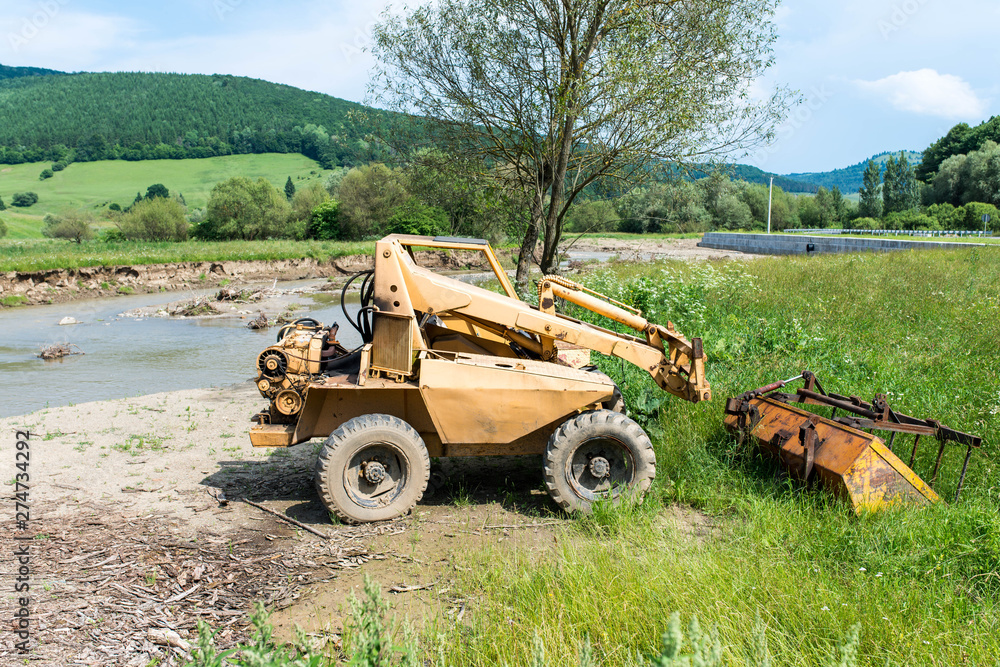 Obraz premium Abandoned ,old mini excavator near a small river.