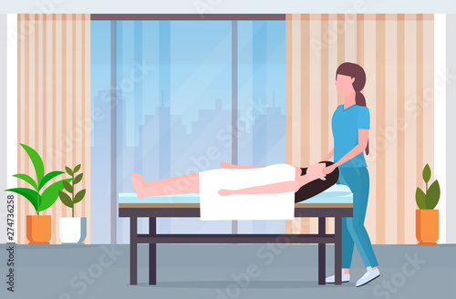 woman lying on massage bed african american masseuse doing healing treatment massaging injured patient manual physical therapy rehabilitation concept modern clinic spa salon interior full length