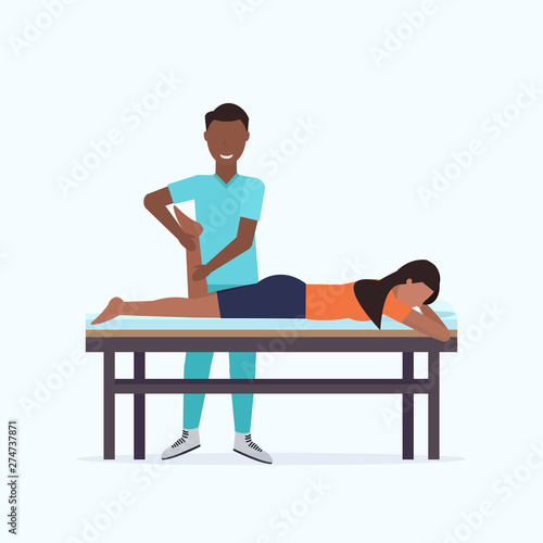 woman lying on massage table african american masseur therapist doing healing treatment massaging patient injured leg manual sport physical therapy rehabilitation concept full length