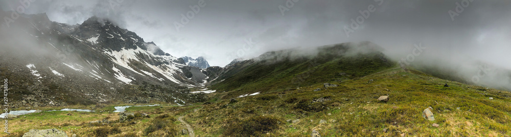 Panoramic view of an alpine valley with low hanging clouds