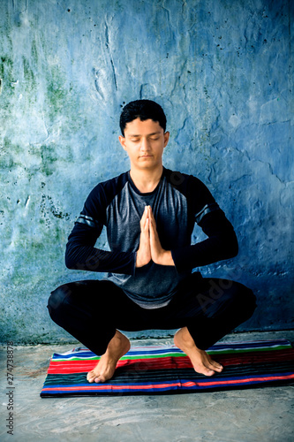 Teenage boy wearing black colored attire and doing yoga on colorful traditional mat and doing famous Garland pose or Malasana. Vertical shot. photo