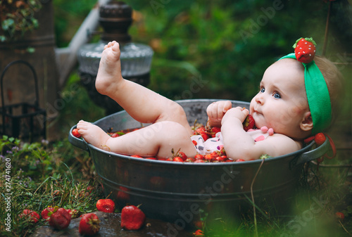 A little girl bathes in a basin with strawberries in the garden.