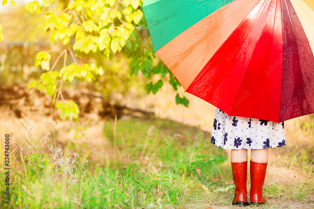 Happy child girl walk with multicolored umbrella under rain