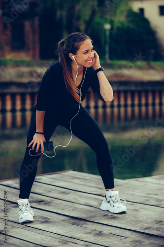 Attractive young woman taking break after jogging while listening to music on her smart phone