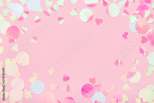 Festive frame of iridescent multicolored confetti sparkling on pink pastel background. Trendy holiday backdrop. Flat lay, copy space.