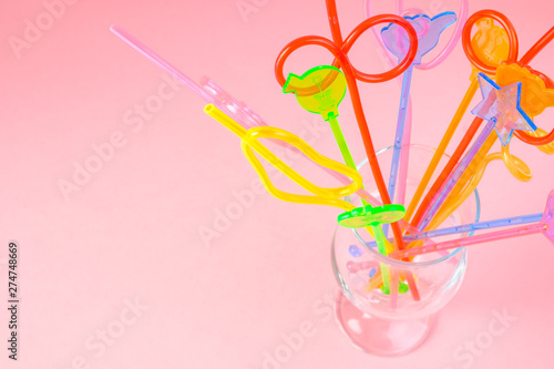 Multicolored plastic cocktail straws in an empty glass cup on a pink background. Concept: holiday, party, ecology, plastic