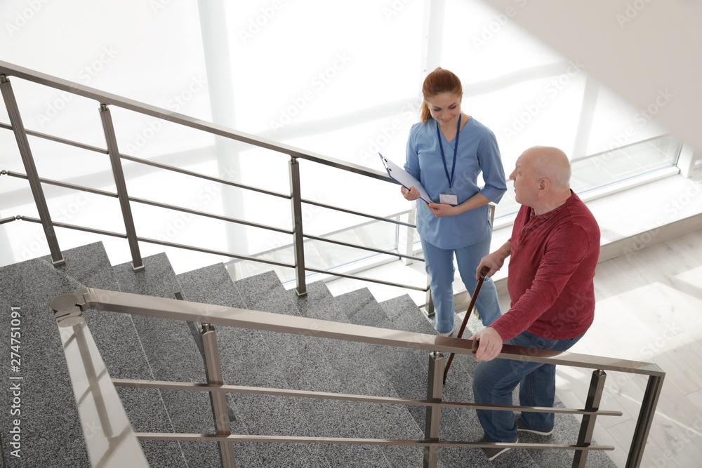 Nurse assisting senior man with cane to go up stairs indoors