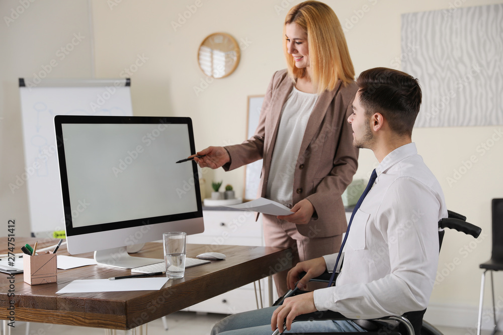 Obraz premium Man in wheelchair with his colleague at workplace