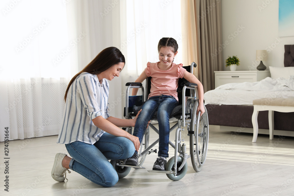 Young woman helping her disabled daughter get in wheelchair at home Young woman helping her disabled daughter get in wheelchair at home