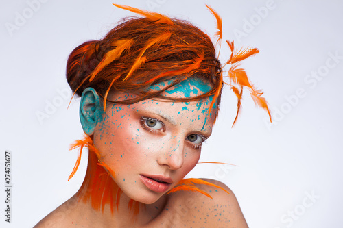 Portrait of a beautiful model with creative make-up and hairstyle using orange feathers