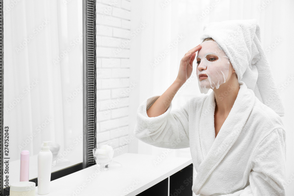 Beautiful woman with sheet mask on her face at mirror indoors Beautiful woman with sheet mask on her face at mirror indoors
