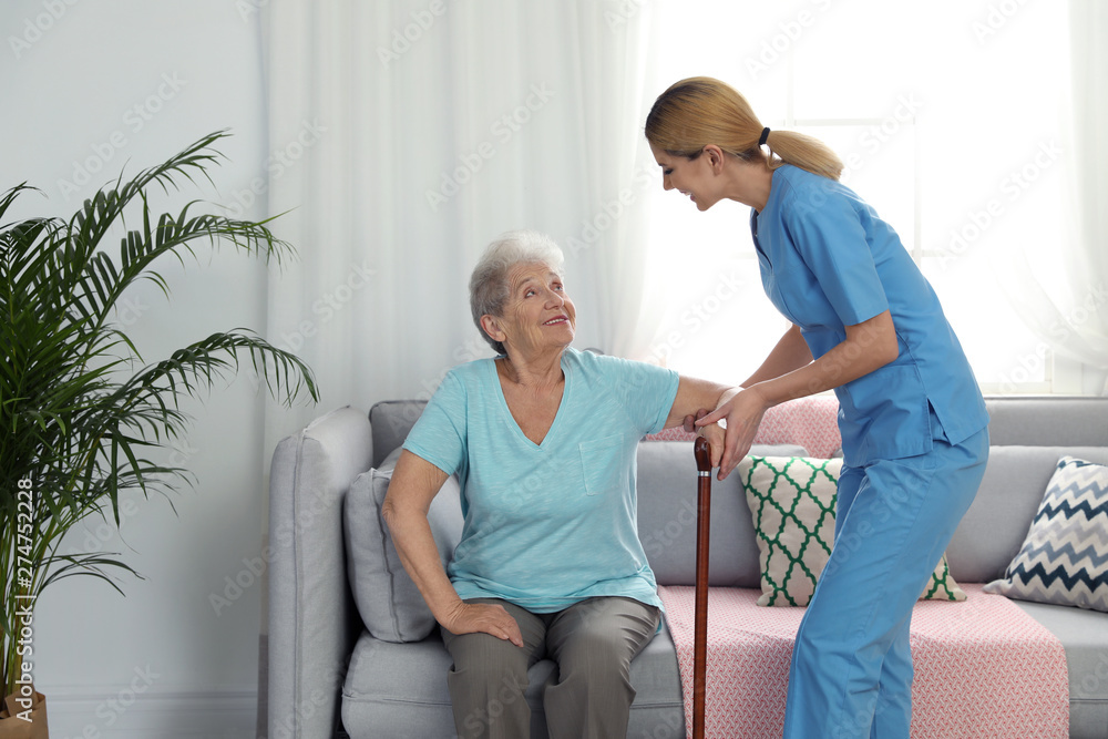 Fototapeta premium Nurse assisting elderly woman with cane indoors