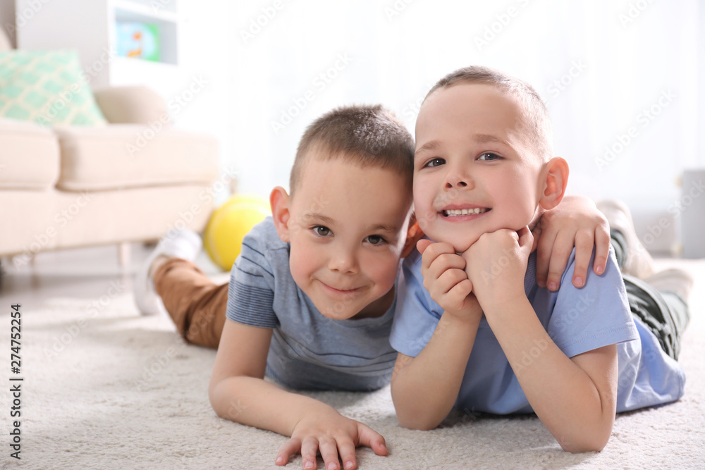 Portrait of cute twin brothers on floor in living room - obrazy, fototapety, plakaty 