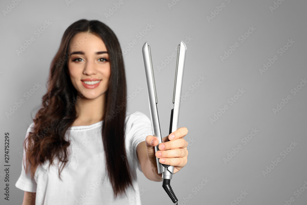 Happy woman with hair iron on grey background. Space for text Happy woman with hair iron on grey background. Space for text