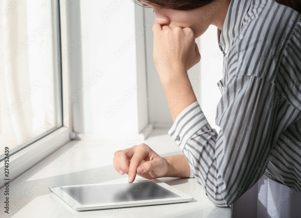 Young woman using tablet near window indoors, closeup with space for text. Loneliness concept Young woman using tablet near window indoors, closeup with space for text. Loneliness concept