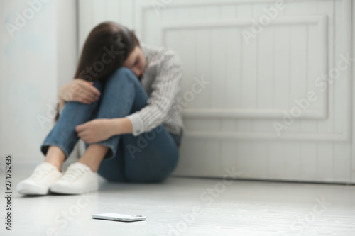 Lonely woman sitting on floor and smartphone on foreground, space for text