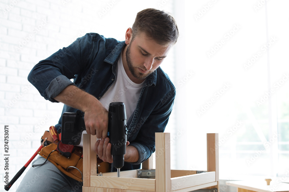 Young man working with electric screwdriver indoors. Space for text Young man working with electric screwdriver indoors. Space for text